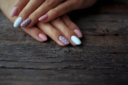 Women is hands with a beautiful manicure on a wooden background. Autumn trend, polish beige and white polka dots on nails with gel polish, shellac. copyspace.の写真素材