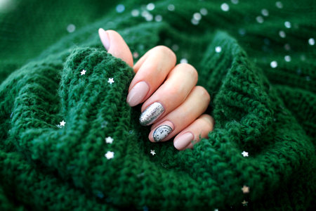 Beautiful female hand in a green sweater with Christmas nail design. Nail design, manicure with chimes pattern. Shellac, gel polish.の写真素材