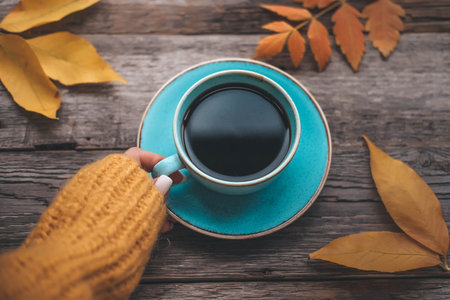 Girl's hand holds a cup of coffee on a wooden autumn background. Tea and autumn leaves on a wooden background.の写真素材