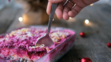 Homemade New Year is a herring salad under a fur coat on a wooden background. A man's hand lays a Russian traditional Christmas salad with a spoon.の写真素材