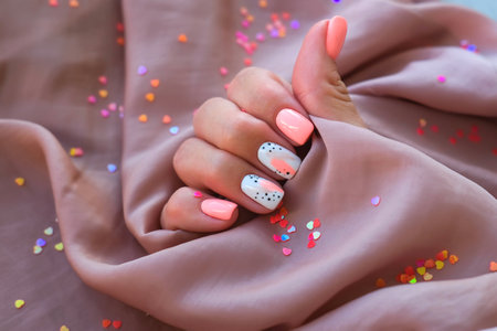 Women - a hand with a beautiful manicure holds a silk fabric on a background of sparkles. Pink trend, polishing the pattern on the nails with gel polish, shellac. holidayの写真素材
