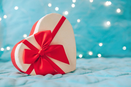 Beautiful holiday box in the shape of a heart with a red ribbon on a background of blur garlands. Christmas. Valentine's Day. copyspace. February 14の写真素材