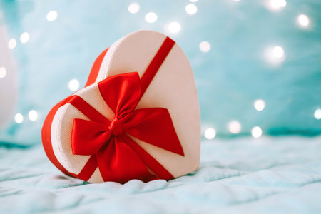 Beautiful holiday box in the shape of a heart with a red ribbon on a background of blur garlands. Christmas. Valentine's Day. copyspace. February 14の写真素材