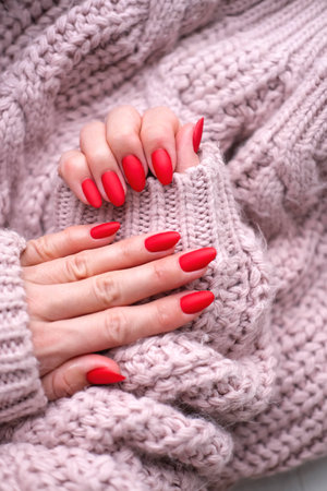 Women's hands with a beautiful matte oval manicure in a warm pink knitted sweater. Winter trend, cover red nails with gel polish, shellac. copyright.の写真素材