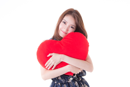 Asian woman holding a red heart-shaped pillow.の写真素材