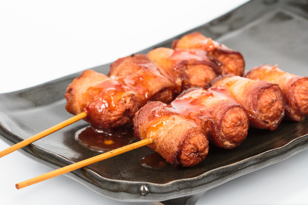 fried sausage rolled with bacon on black plateの写真素材