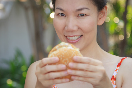 Asian girl eating a hamburger in a swimsuit.の写真素材