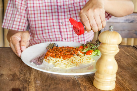 man putting oregano in spaghetti and pepper
