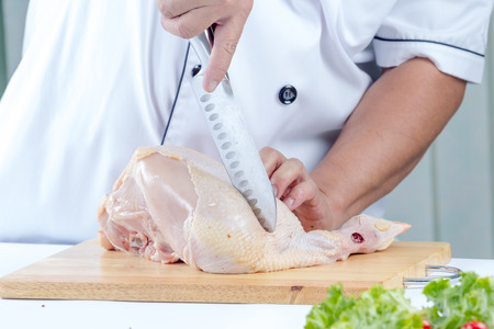 chef with knife cutting raw chicken in the kichenの写真素材