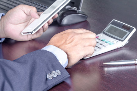 Businessman using a calculator and holding smartphone