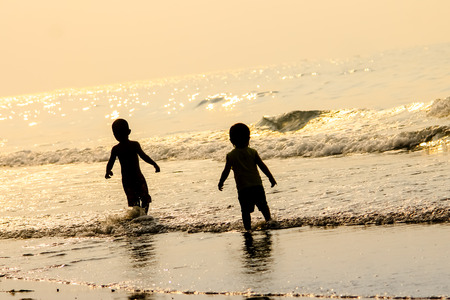 Two children play in the sea at sunset timeの写真素材