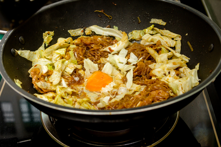 chef cracking an egg into fried noodle in pan for thai food menuの写真素材