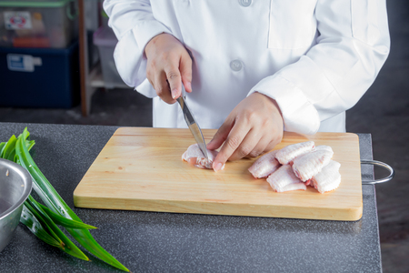 chef cutting raw chicken wing on chopping boardの写真素材