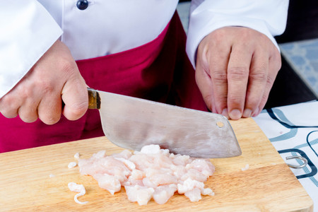 chef with knife sliced raw chicken on wooden boardの写真素材