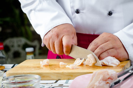 chef with knife sliced raw chicken on wooden board