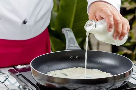 chef pouring milk in pan for making spaghettiの写真素材
