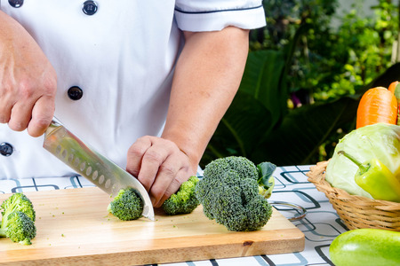 chef cutting fresh green broccoli on a wooden boardの写真素材