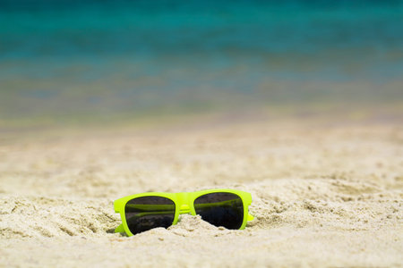 yellow children's sunglasses in the sand against the background of the seaの写真素材