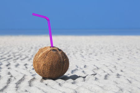 peeled coconut with a straw in the sand on sea backgroundの写真素材