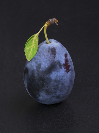 Ripe plum with a green leaf isolated on a black backgroundの写真素材