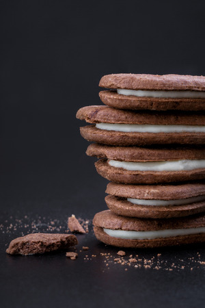 Chocolate sandwich cookies with white cream filling on a black background, close-up side viewの写真素材