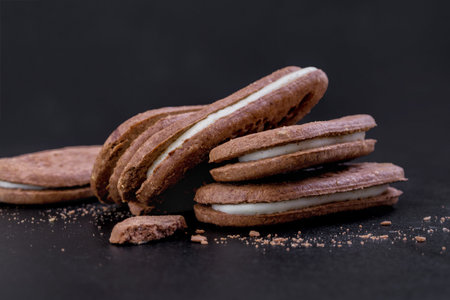 Chocolate sandwich cookies with white cream filling on a black background, close-up side view