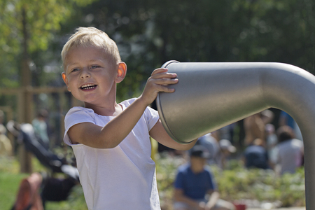 A little boy is talking in a metal pipe for talks in the playground on a sunny summer dayの写真素材