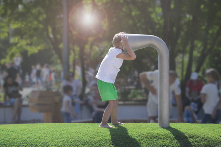 A little boy is talking in a metal pipe for talks in the playground on a sunny summer dayの写真素材