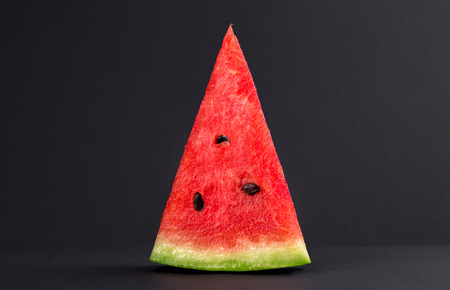 Triangular piece of ripe watermelon with black seeds on a black background close-up macro shotの写真素材