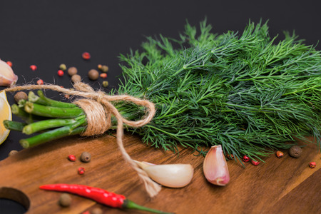 A bunch of fresh dill bandaged with a rope with a bow and a mix of spices and garlic on a black board, top viewの写真素材