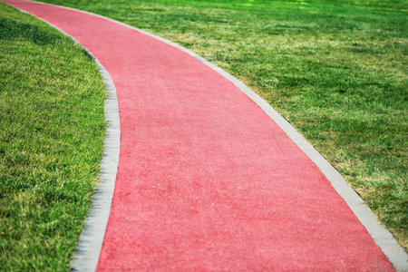 A red soft jogging track in the park turns in the grass on a sunny summer dayの写真素材