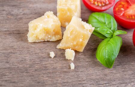 Pieces of Italian Parmesan Reggiano with green basil and tomatoes on a wooden boardの写真素材