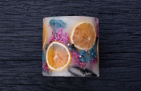 Large aromatic decorative candle with a herbarium of dried herbs and fruits inside on black wood backgroundの写真素材