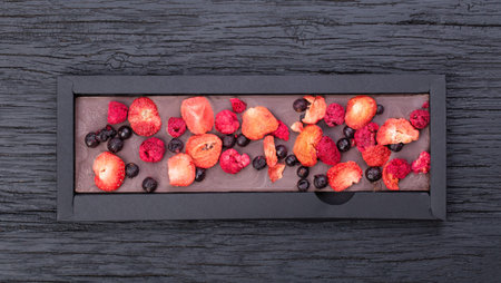 Handmade chocolate bar with dried berries in black cardboard craft packaging on a wooden black table