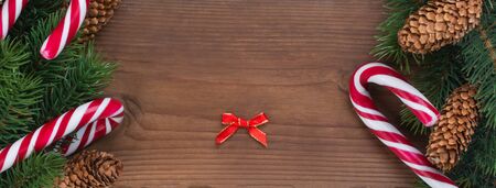Empty greeting card for Christmas. Christmas tree branch decorated with garlands, cones and caramel sticks on a brown wooden table background, top viewの写真素材