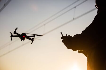 silhouette of a man operating drone close to the electrical wire/ man holding remote control drones/drone controller.の写真素材