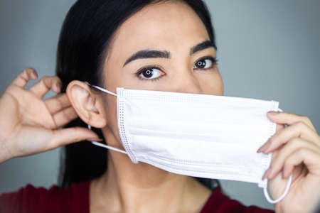 A woman putting on a medical disposable mask to avoid contagious viruses.の写真素材