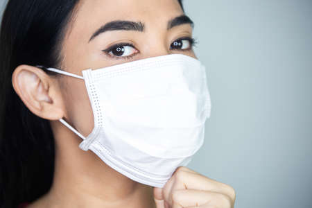 A woman putting on a medical disposable mask to avoid contagious viruses.の写真素材