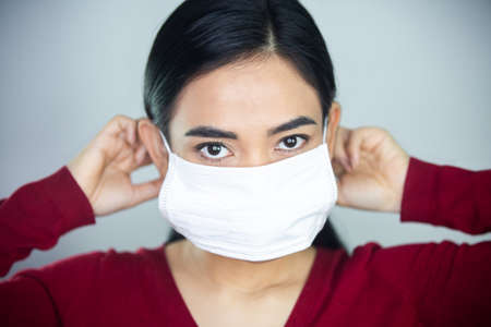 A woman putting on a medical disposable mask to avoid contagious viruses.の写真素材