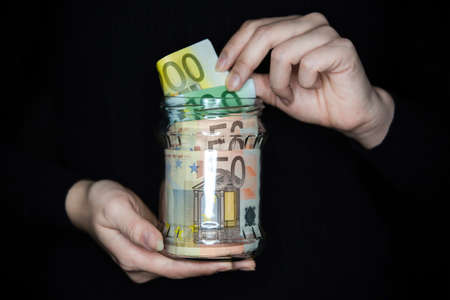 Woman holding a jar full of money. Woman pulling money out of the jar. Saving money in a jar.の写真素材