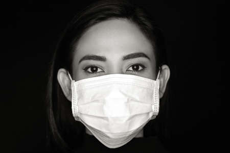 Coronavirus outbreak concept: An Asian woman putting on a medical disposable mask to avoid contagious viruses. Black and white photo.の写真素材