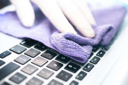 Hand with protective gloves cleaning a computer keyboard. Cleaning laptop keyboard to eliminate germs, bacteria, and viruses. Stay at home. Preventing Coronavirus.の写真素材