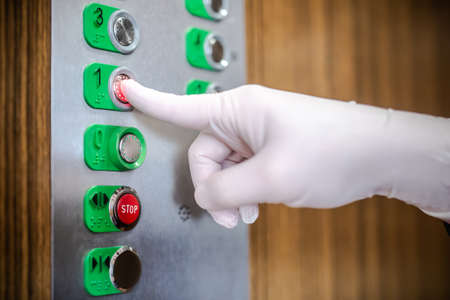 coronavirus outbreak : Hand wearing rubber white glove pressing elevator buttons. hygiene concept : bacterias and viruses prevention. Preventing coronavirus transmission. Self-protection.の写真素材