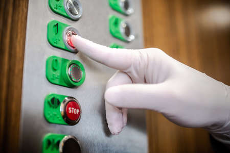 coronavirus outbreak : Hand wearing rubber white glove pressing elevator buttons. hygiene concept : bacterias and viruses prevention. Preventing coronavirus transmission. Self-protection.の写真素材