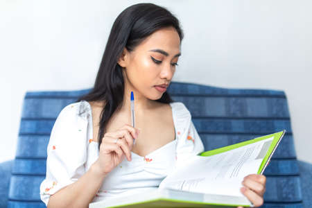 Beautiful Asian woman-focused studying / reading a book at home. Studying remotely.の写真素材