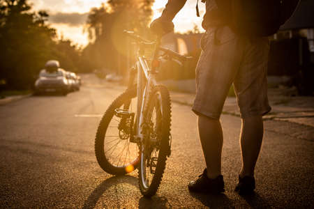 A man standing next to a bicycle in the middle of the road, with a sunset viewの写真素材