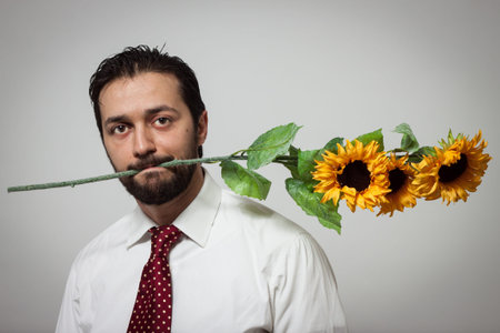 Portrait of a young bearded man with sunflowers in his mouthの写真素材