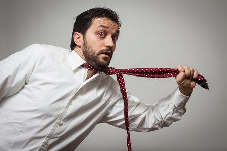 Young bearded man with red tie pulling himself on grey backgroundの写真素材