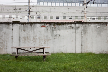Table and bench in the grass close to a grey wall limiting the railroadの写真素材
