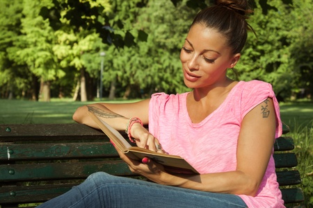 Portrait of a beautiful girl reading book on benchの写真素材